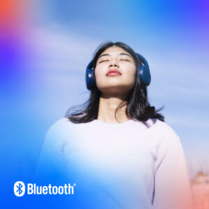 Young woman with blue Bluetooth headphones enjoying music against a serene blue sky.